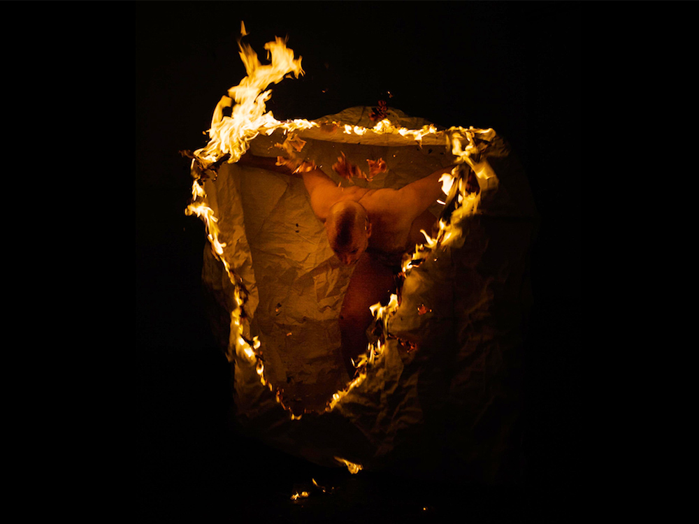 Person emerging through ripped material on fire