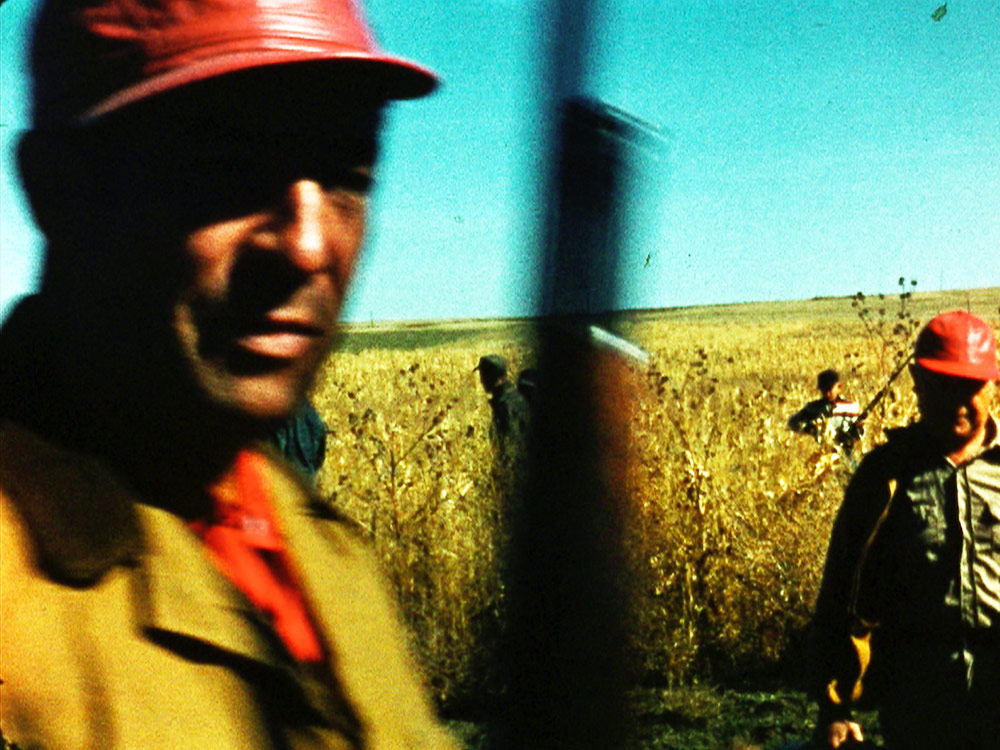 Black man working in wheat field, other workers behind