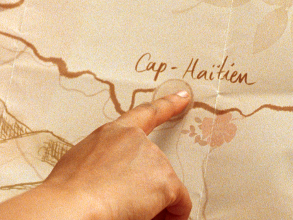 A hand points to a location on a paper map marked Cap-Haitien