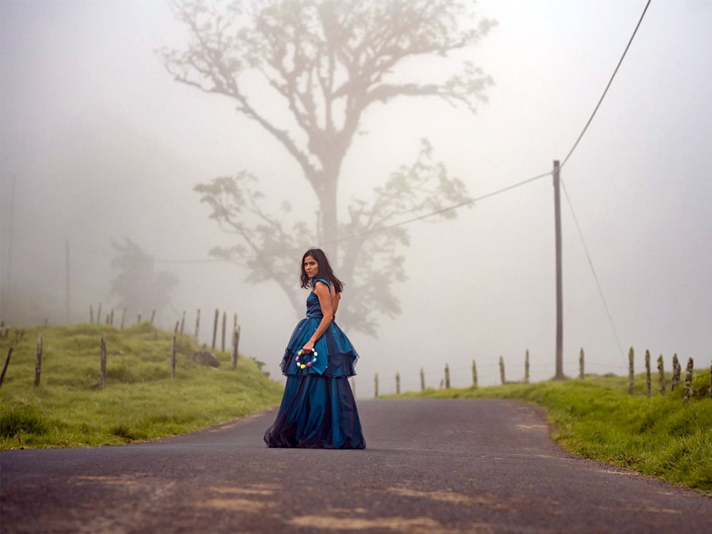 A person in a blue dress stands against a foggy, empty road