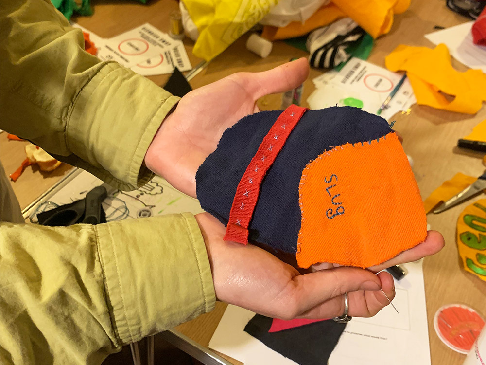Two hands hold pieces of material that read 'SLUG'. There are bits and pieces of material scattered in the background, the pieces of a workshop.