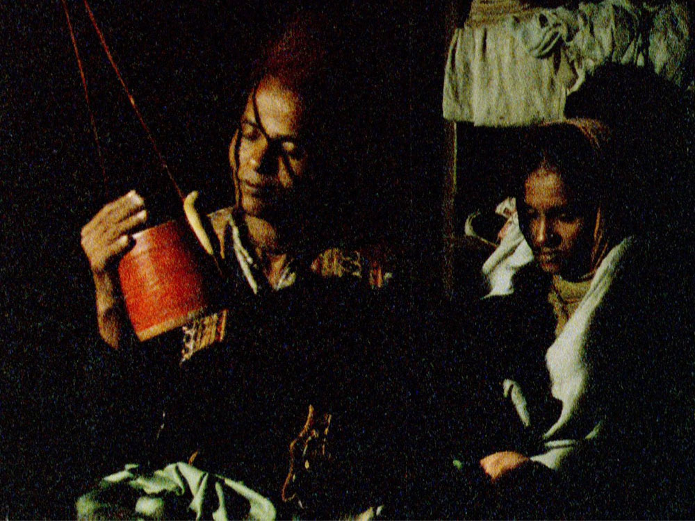 Two people, in low light, look at a red piece of pottery