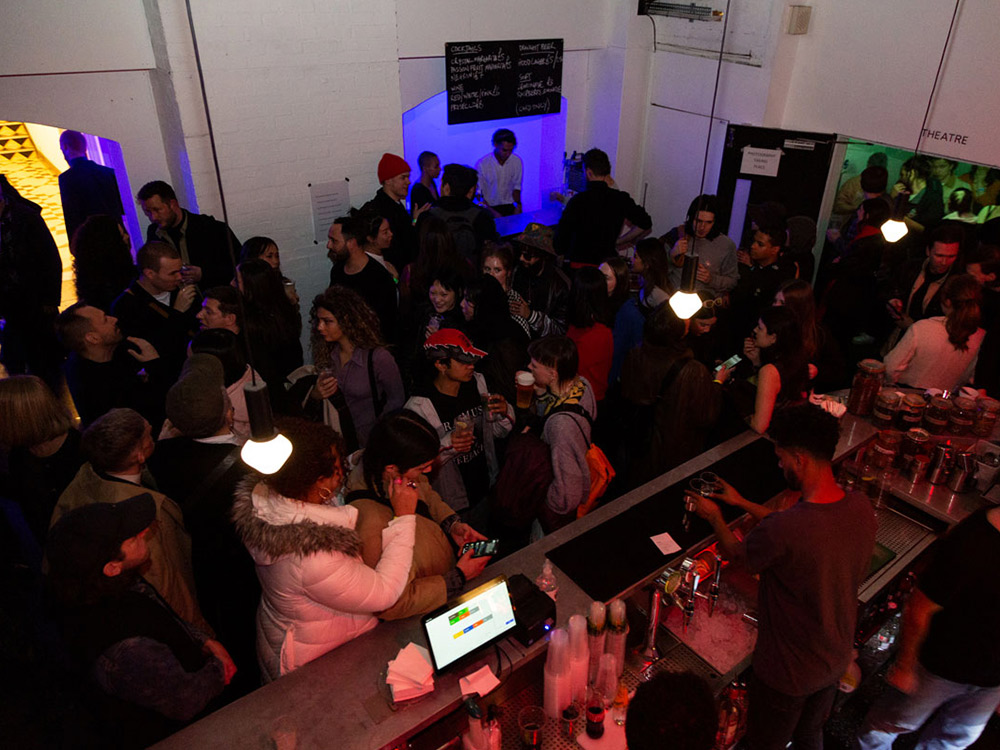 An overhead shot of a crowd gathering at the ICA Bar. There are coloured lights filling the room.