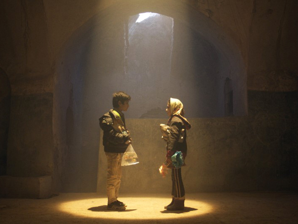 Two young people stand in an old stone building under a spotlight