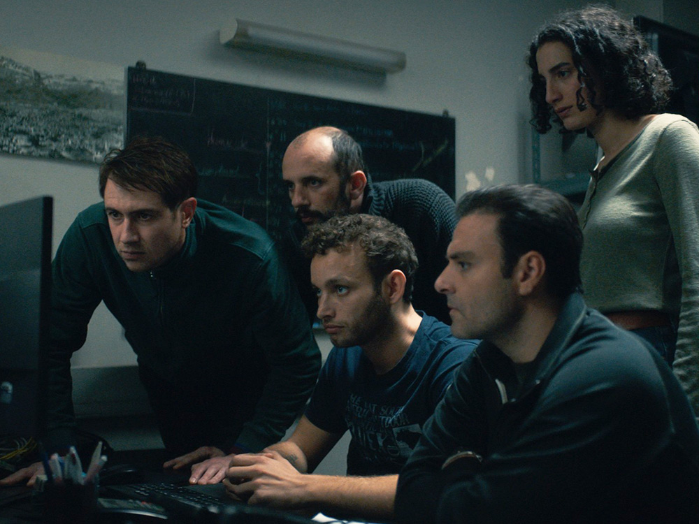 A group of people crowd around a single computer screen, observing closely