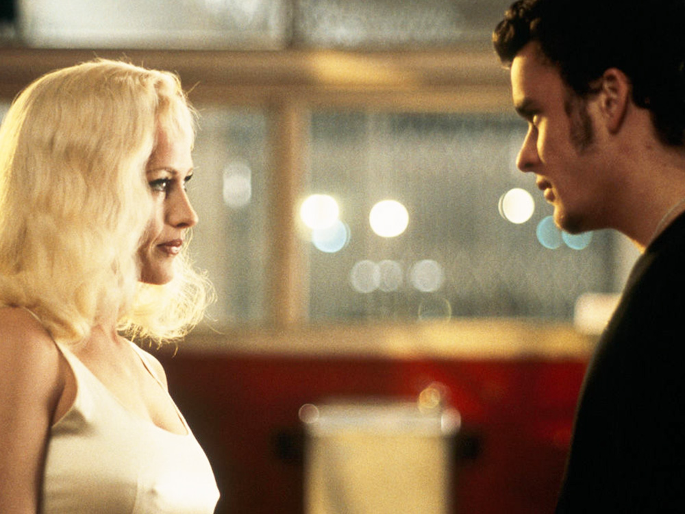 A blonde woman and a young man stare into each other's eyes, mysteriously