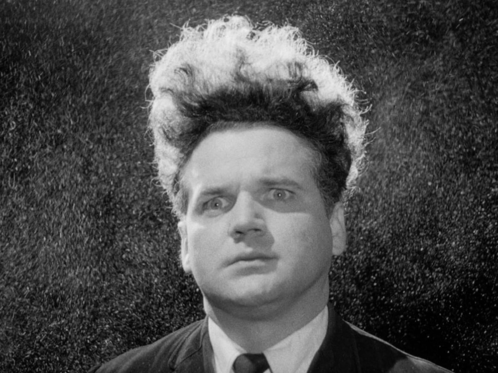 A man in a suit with shocked hair stares, shocked, in black and white