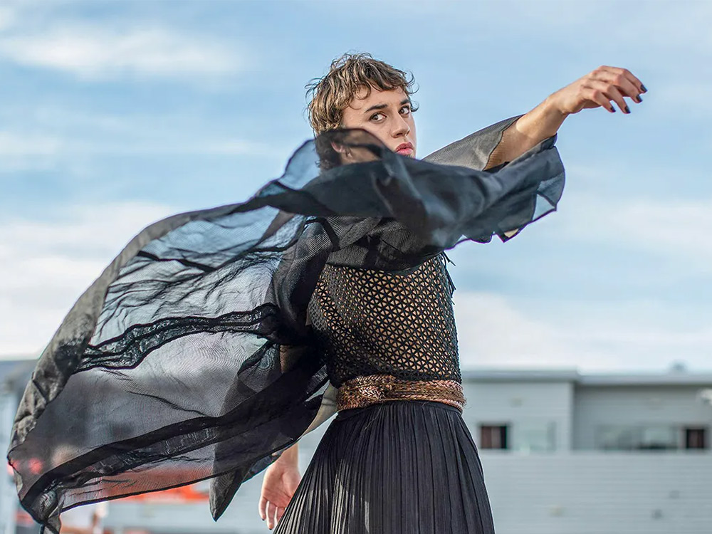 A person wearing mesh and loose flowing black silk poses in the wind
