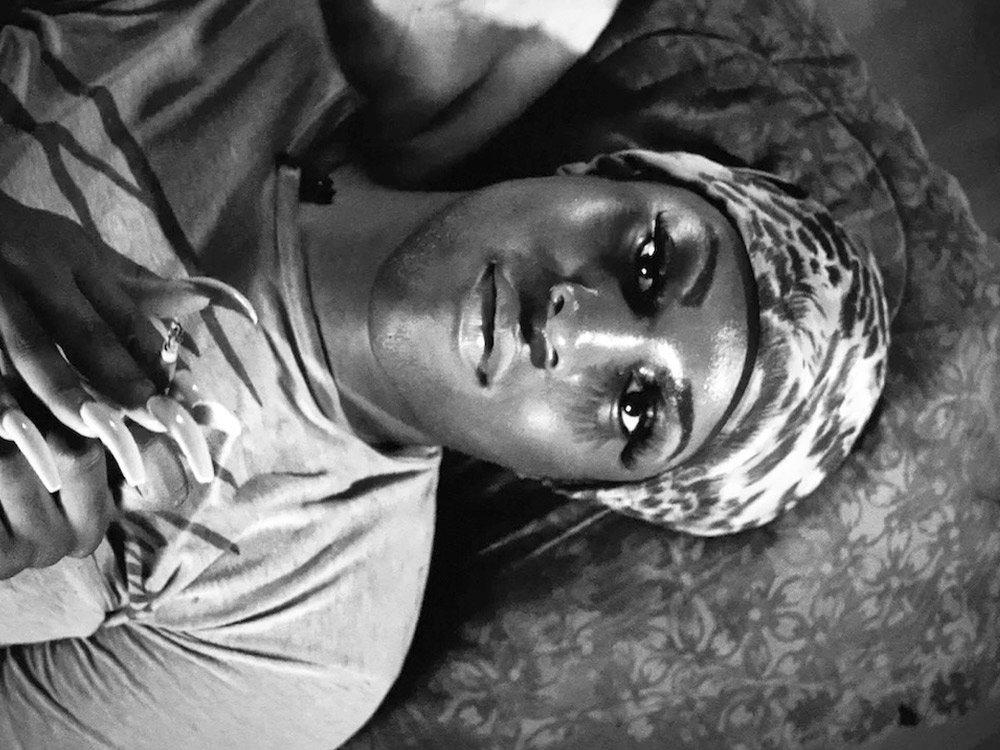 In black and white, a black woman lying on the couch staring at the ceiling. She has manicured nails