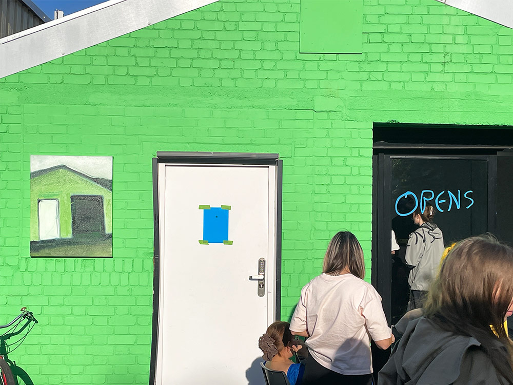 People gather outside a green-walled house. The window reads 'Open' in blue text