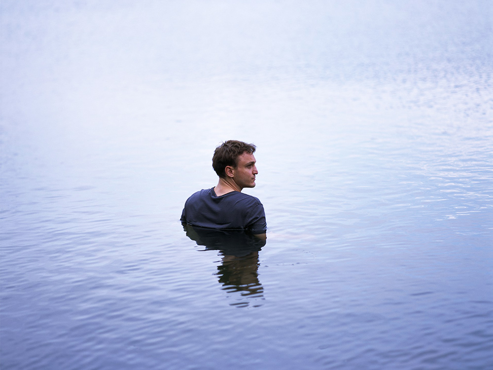 A man wades through steely blue water, the water up to his chest