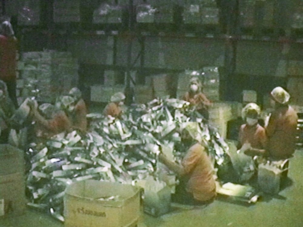 Grainy image of factory workers packing mangosteen juice into silver packets