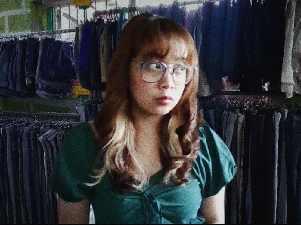 A Filipino woman with glasses stands in front of racks of denim shorts and jeans