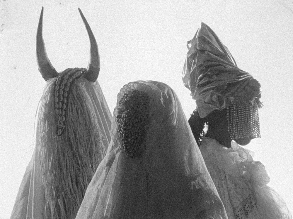 A black and white photo of three figures in masks and headdresses