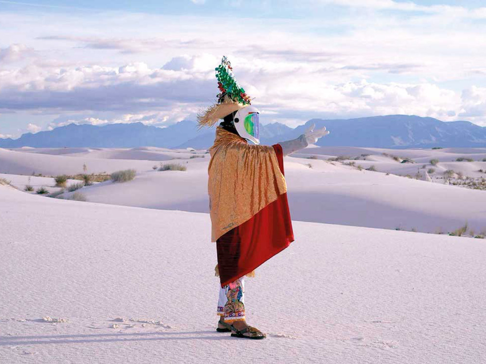 An alien-like Nahua traveller in a snow mask and traditional clothing stands in a field of snow