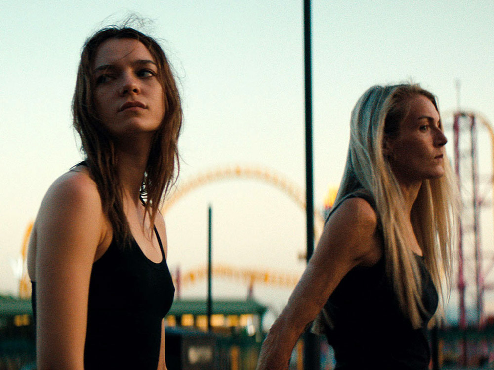 Two women stand in an amusement park, looking lost