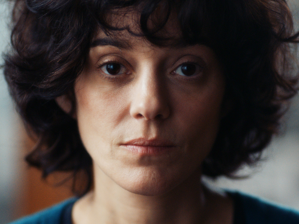 A woman with curly hair stares blankly