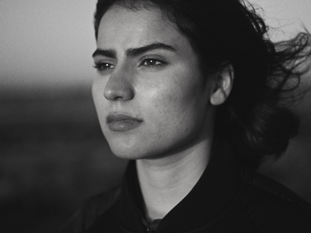 A black and white woman of a young Afghan woman with a strong face looking out to the distance, wind blowing her hair