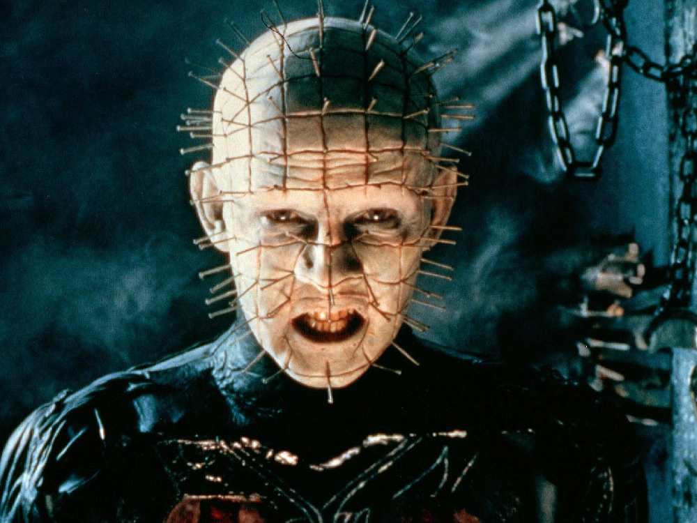 Leader of the 'Cenobites', later known as Pinhead, looks directly to camera, teeth bared, many pins protruding from their face and head