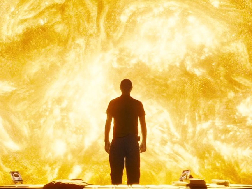 A man stands silhouetted against the sun's surface