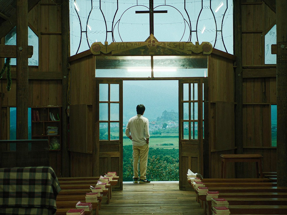 A man stands inside a church door. He looks out to a foggy field in Vietnam