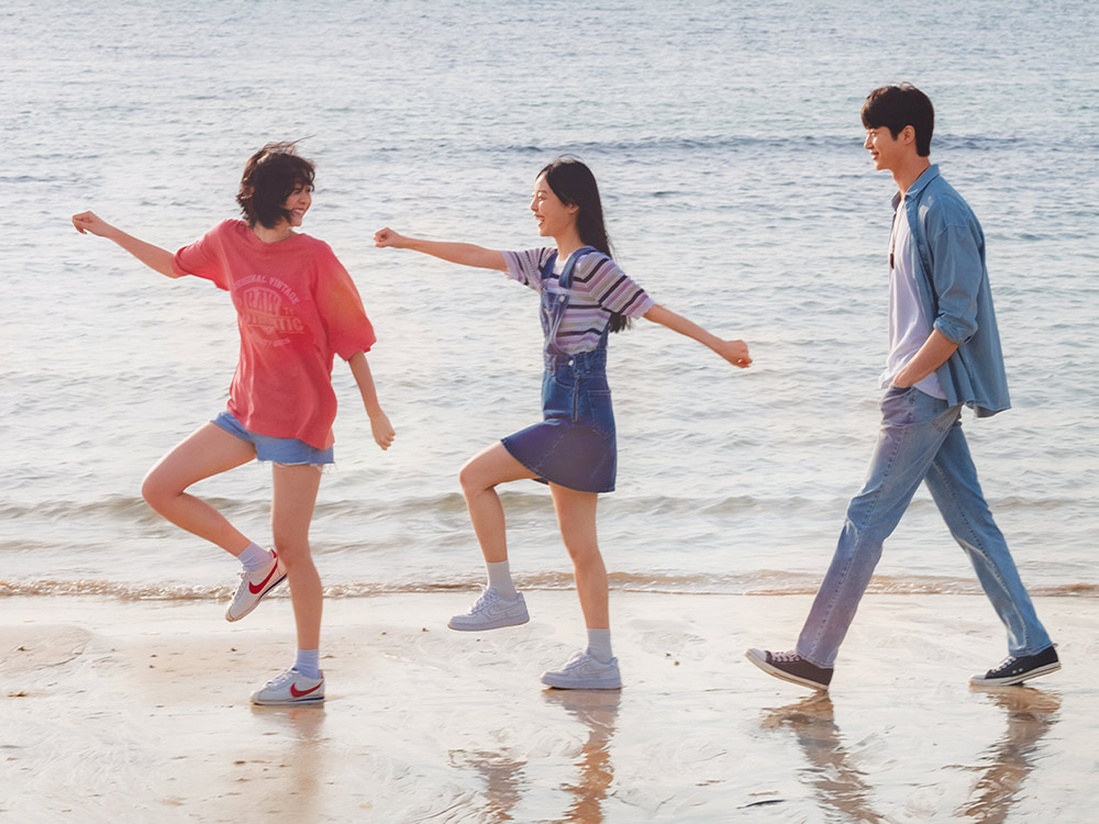 Three people walk playfully across wet sand at the beach