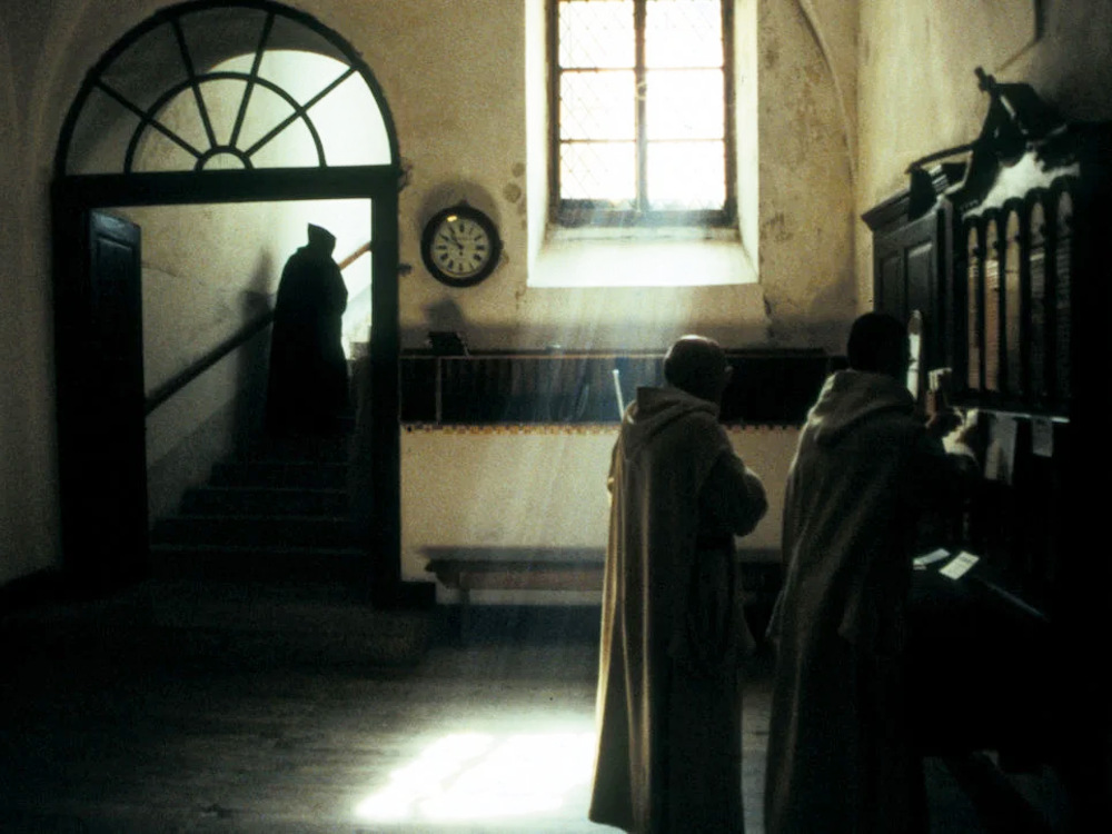 Robed monks carry on their duties in a dimly lit hall