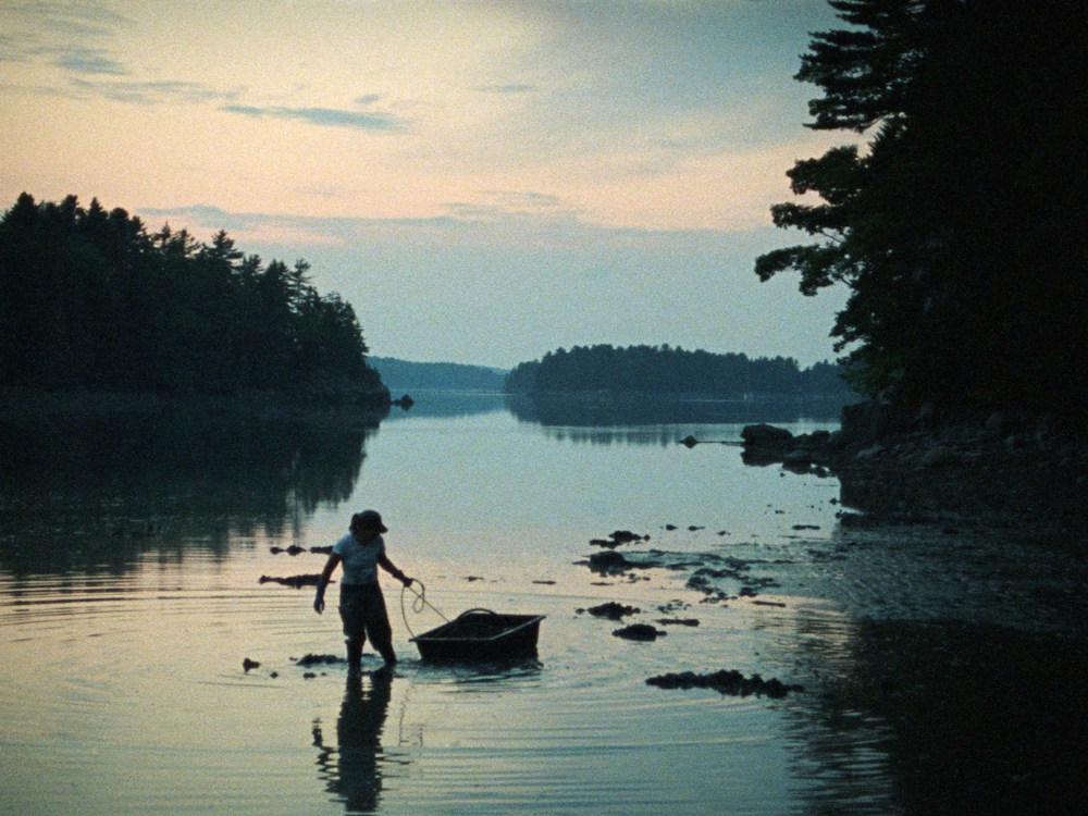 A clam digger drags their boat through a beautiful river under dawn light