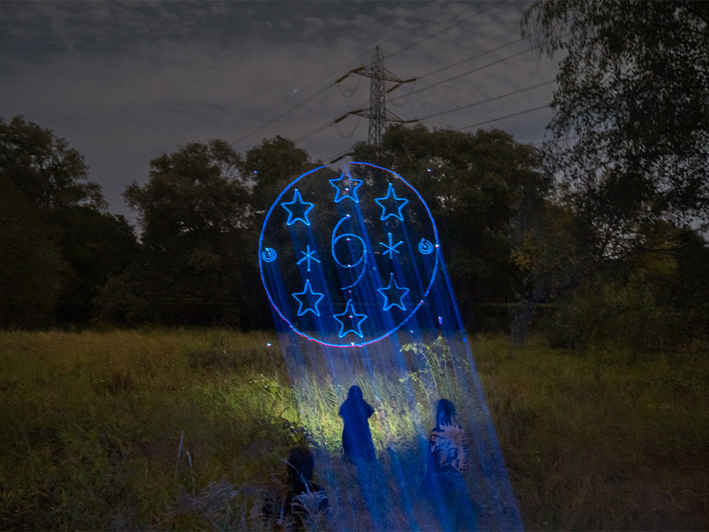 A sigil with stars is projected in blue over a grassy field