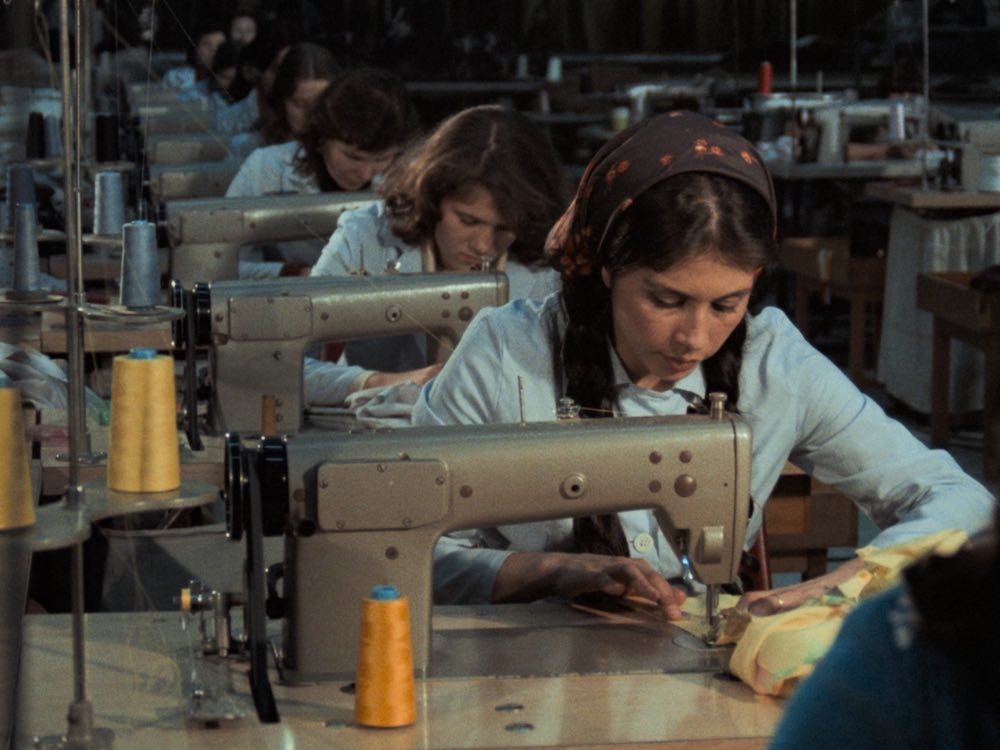 A row of women work on sewing machines in a factory line