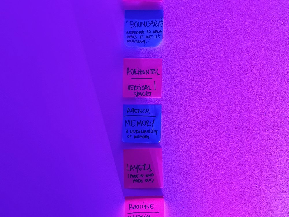 Coloured sticky notes on a wall under purple light, casting shadows