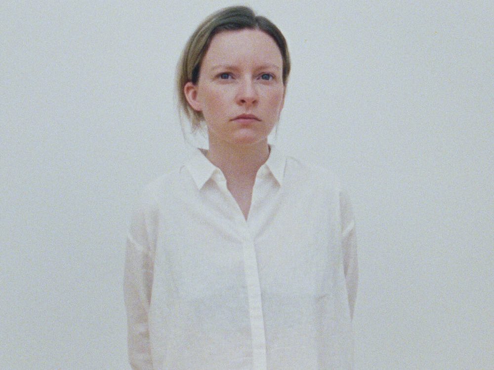 A person in a white shirt with short brown hair stands in front of a white background