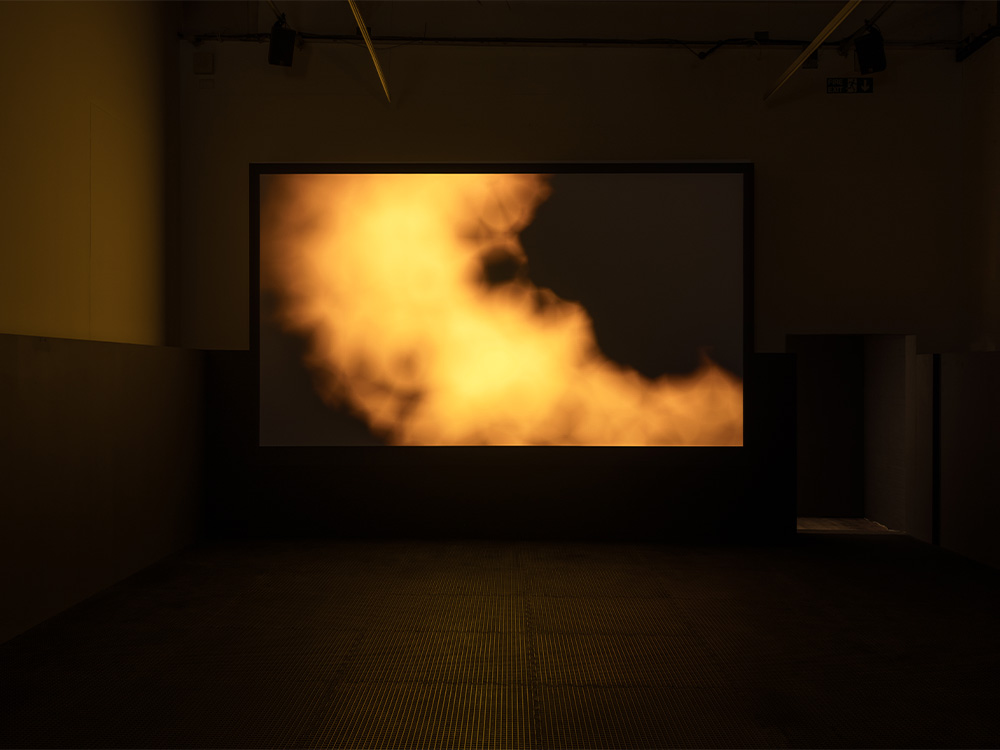 A yellow cloud of smoke disperses on a black background, in a darkened room